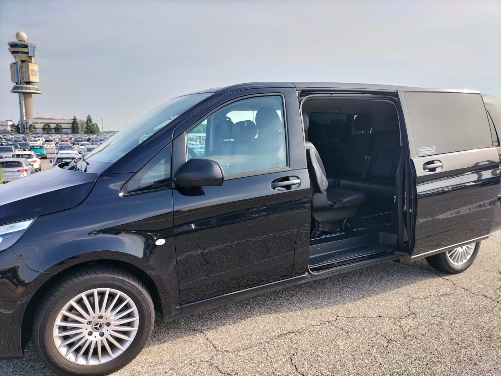 Black minivan with sliding door open, parked in a lot near a control tower.